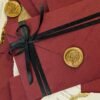 Multiple burgundy wedding cards with deckle-edge gold leaf inserts flat lay
