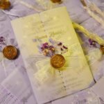 Pastel yellow vellum wedding invitation with gold wax seal and purple dried flowers