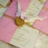 Multiple pink wedding invitations with wax seals and dried flowers flat lay