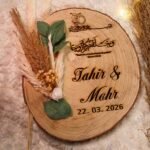 Rustic wood slice nikkah ring tray with laser-engraved Quranic verse, personalized names, pampas grass, and eucalyptus
