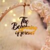 Detail of laser-cut "The Beginning of Forever" wooden sign on golden hoop with roses