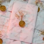 Close-up of white organza bow with gold wax seal and baby's breath